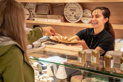 Die Mitarbeiterin vom Chaesbueb Zytglogge überreicht einer Kundin ein Stück Käse zum Probieren. 